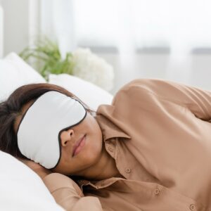 woman in bed, wearing a white sleeping mask. Sleep hygiene, Evoke Wellness Wilmington, NC