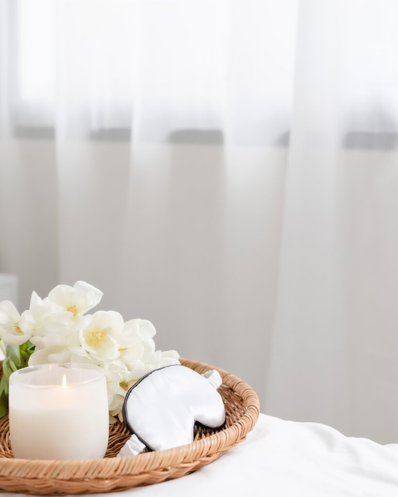 Eye mask, candle, and flowers on a wicker tray on a bed. Sleep hygiene blog from Evoke Wellness Wilmington, NC