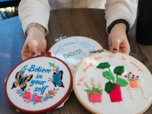 Woman holding needlepoints that have reassuring sayings. New blog from Evoke Wellness "fighting Sunday scaries." Wilmington, NC