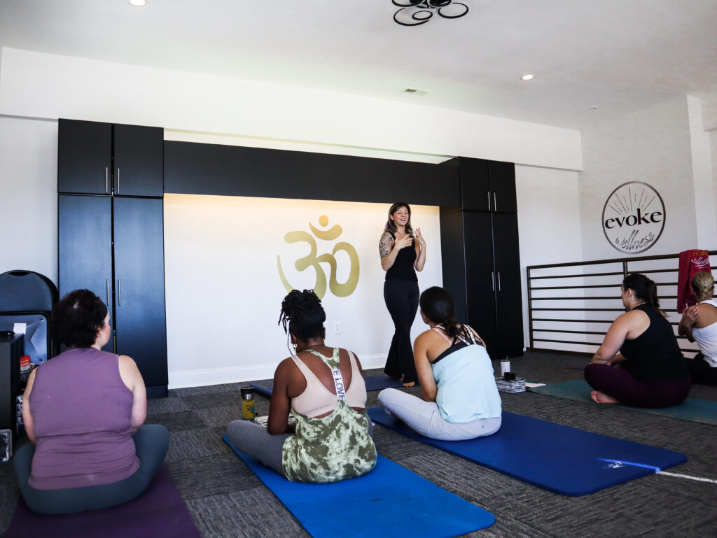 Evoke Wellness yoga instructor Marisa Karoutsos leading a yoga class, several women sitting on yoga mats listening. "Toxic positivity of good vibes only" blog